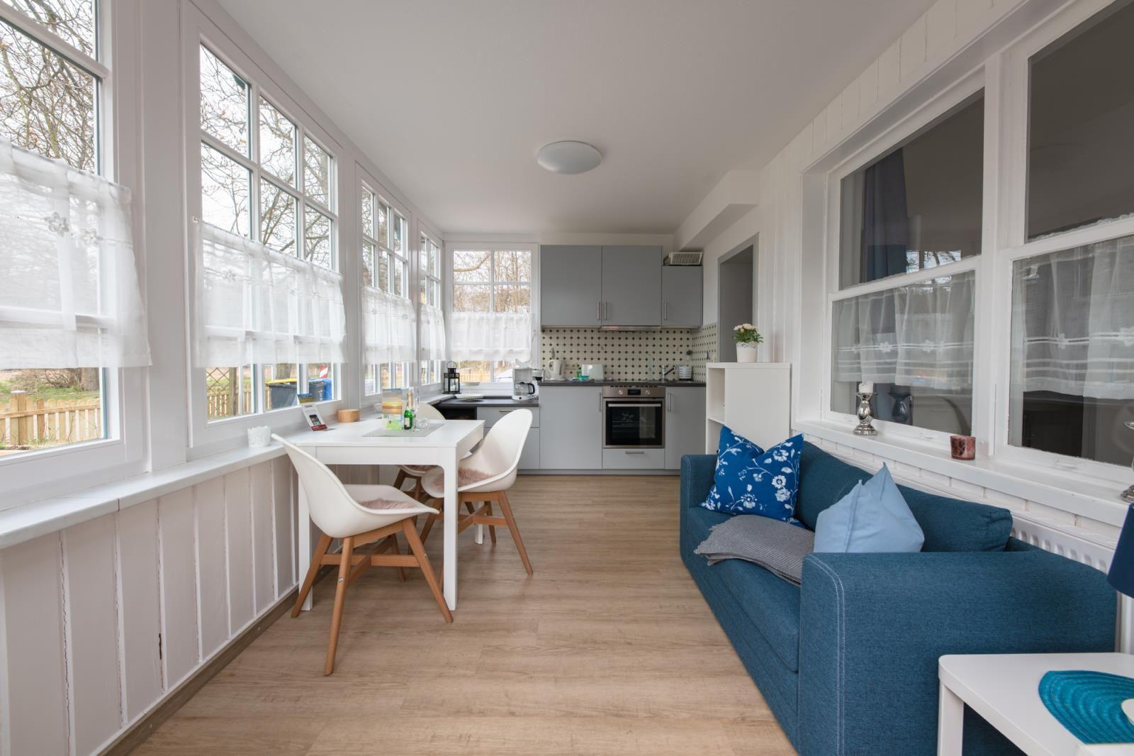 Living kitchen with blue sofa, white table, and large windows.