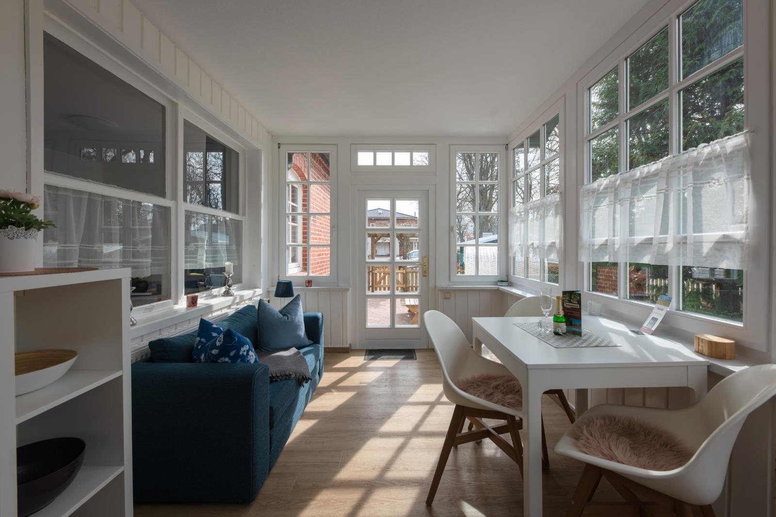 Living and dining area with sofa, table, and chairs. Large windows and door to an outdoor area.