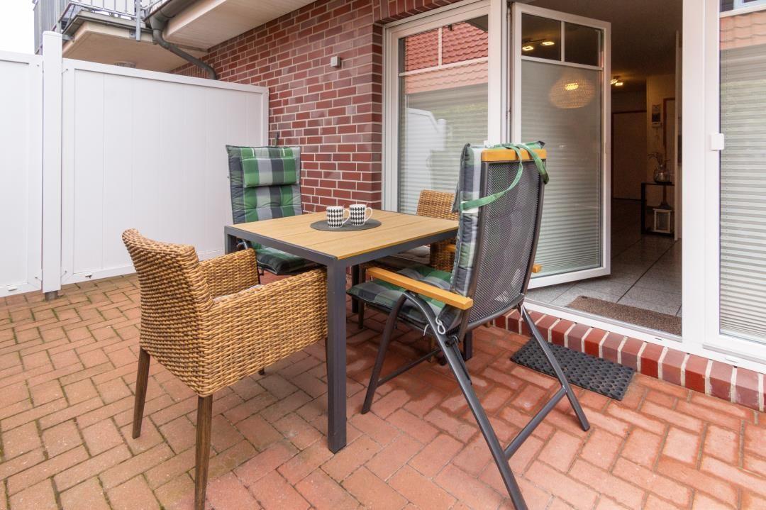 Terrace with table and chairs, glass door to house, red brick paving.