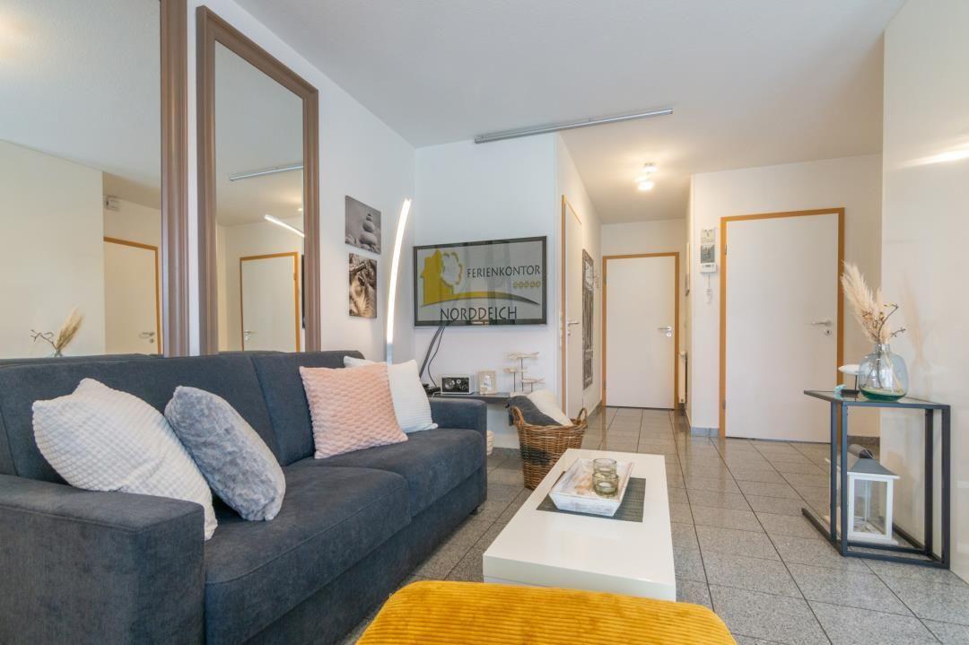 Living room with sofa, coffee table, and TV. Background: hallway and doors.
