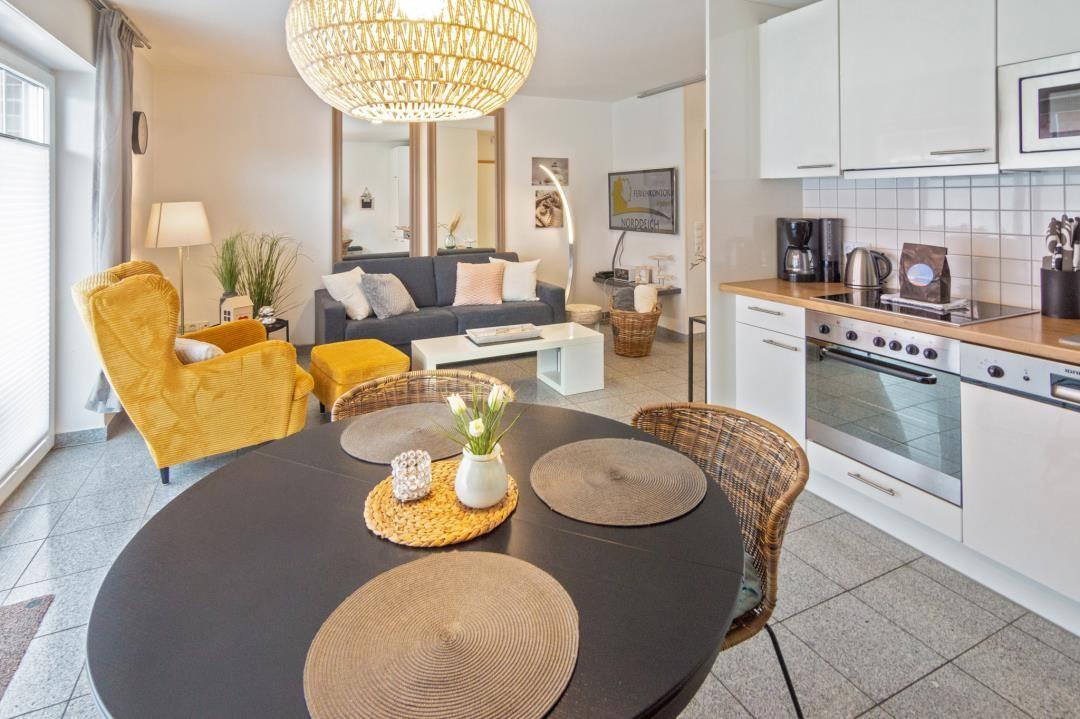 Dining area with round table and chairs, kitchen with white cabinets and living room with sofa and yellow seating.