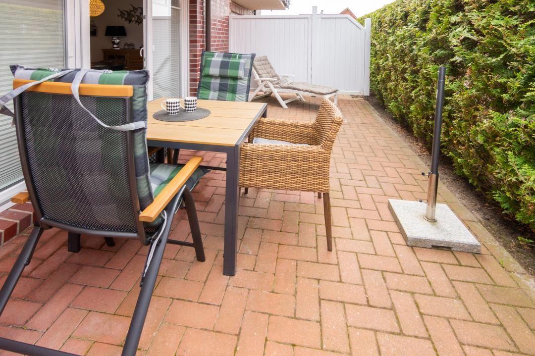 Terrace with table, chairs, and grill area beside hedge.