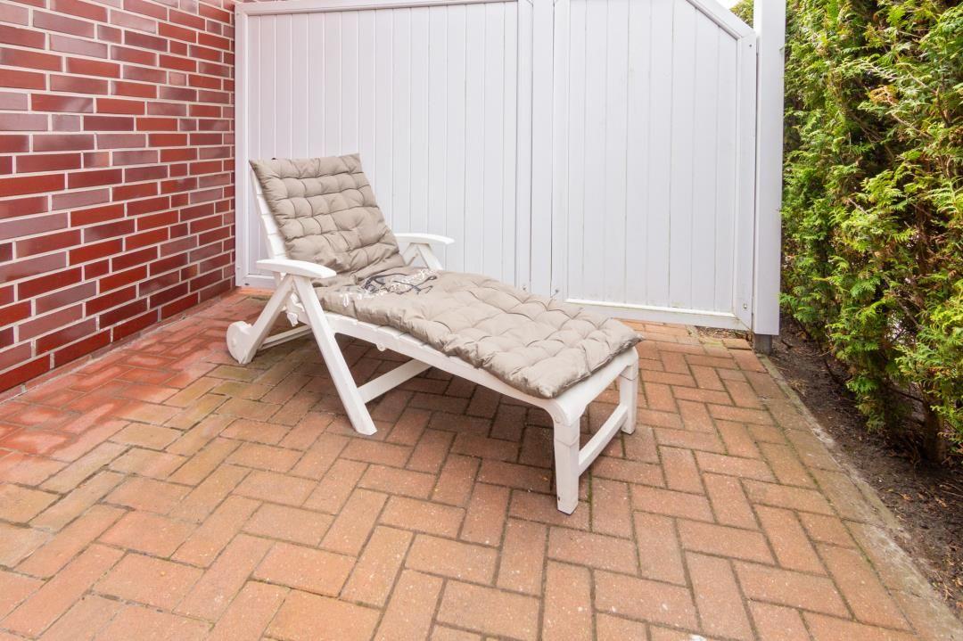 White lounge chair with cushion on terrace next to wall and hedge.