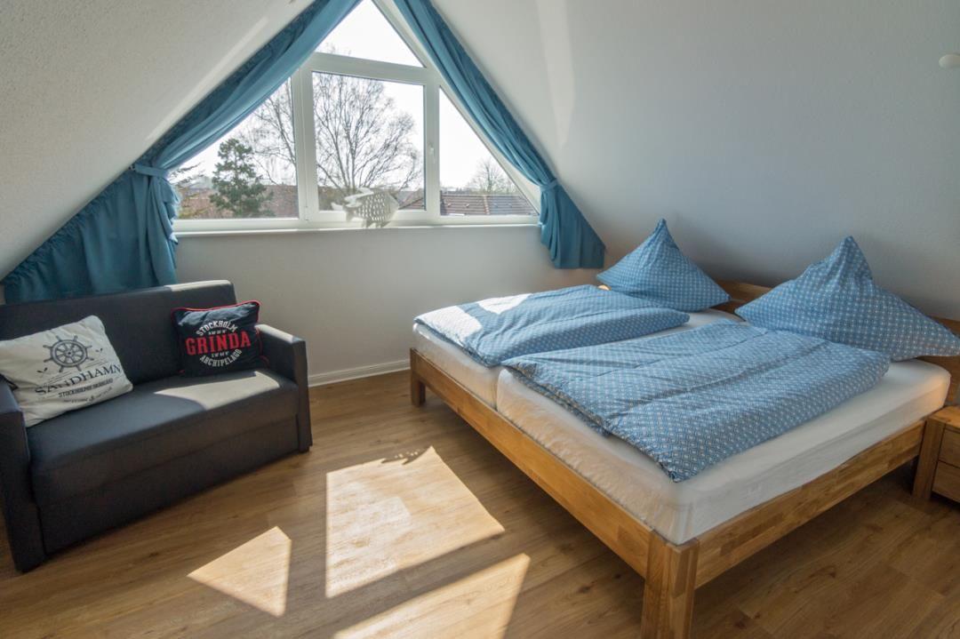 Zimmer mit Doppelbett, Sofa und Dreiecksfenster mit blauen Vorhängen.