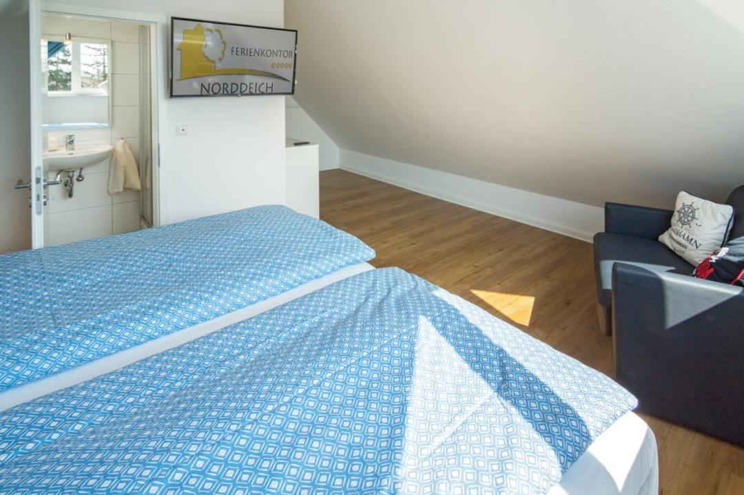 Zimmer mit Doppelbett, Sessel und angrenzender Toilettenstube.