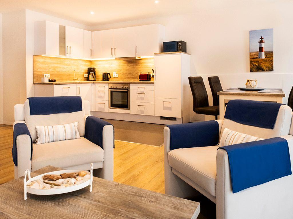 Two chairs with blue covers are in front of a table. Kitchen and dining area are in the background.