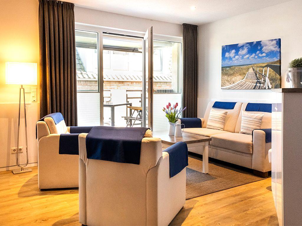 Living room with sofa, armchairs, and terrace. Wall art shows beach.