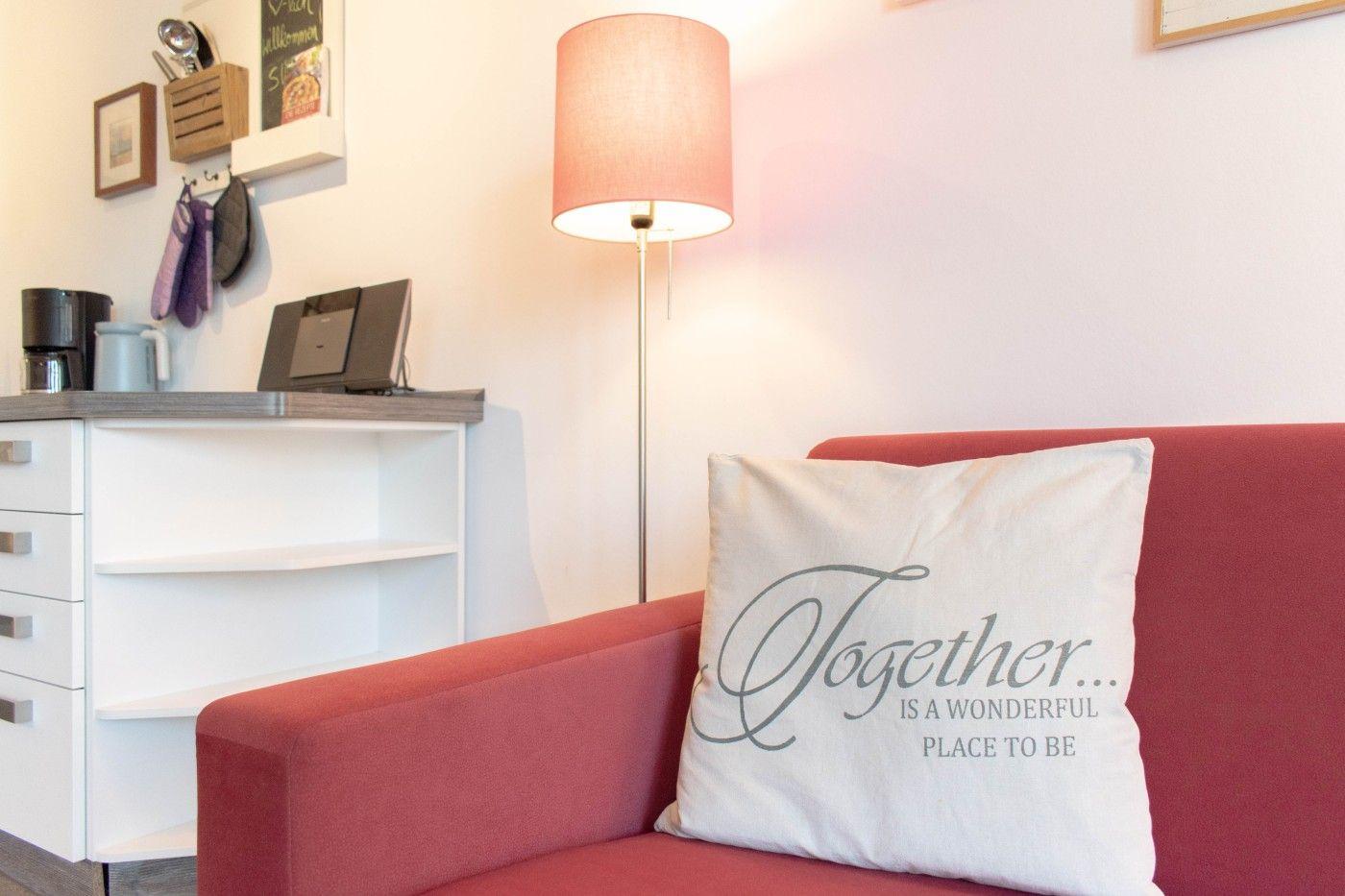 Roter Sessel mit Kissen, Stehlampe und Küchenzeile im Hintergrund.