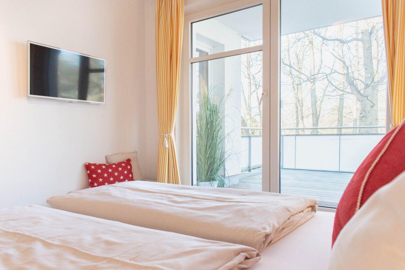 Zimmer mit Doppelbett, TV und Balkon mit Blick auf Bäume.