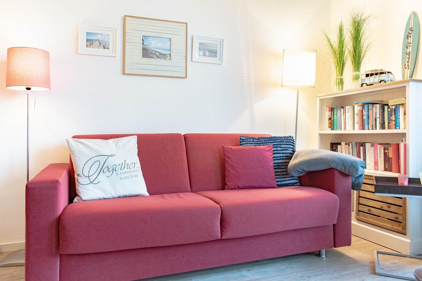 Ein rotes Sofa mit Kissen, Bücherregal und Stehlampen im Wohnzimmer.