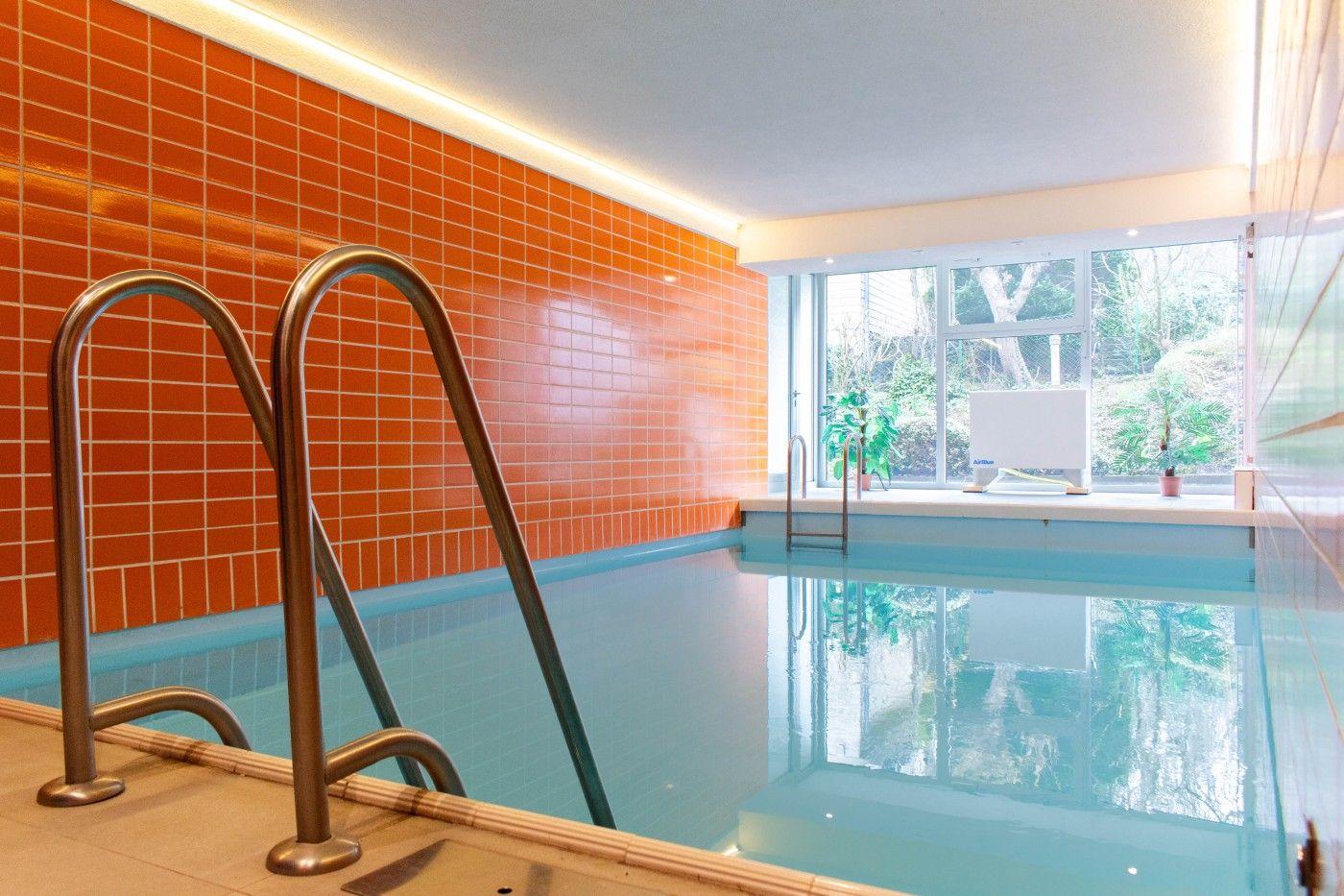 Innenpool mit orangefarbener Wand und Metalltreppe. Fenster zeigt grüne Pflanzen.