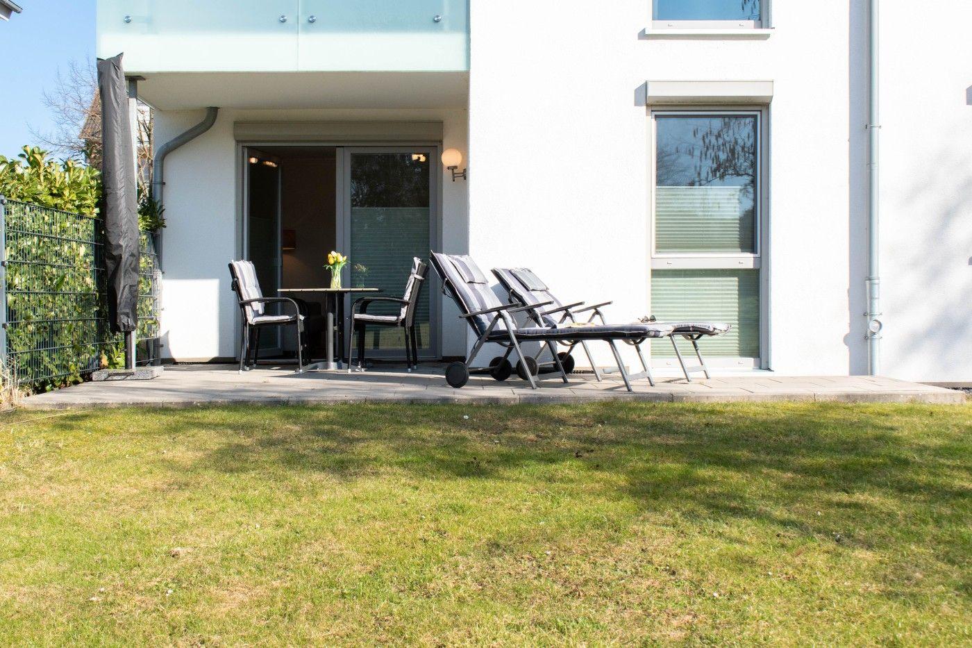 Terrasse mit Liegestühlen und Tisch vor modernem Haus mit grünem Rasen.