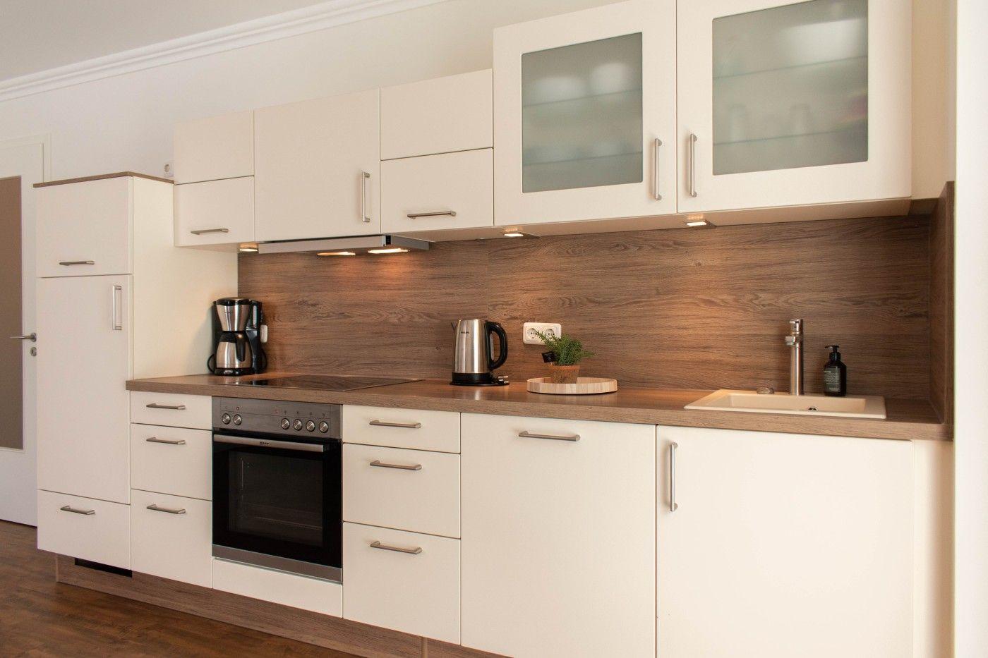 Moderne Küche mit weißen Schränken, Holzrückwand und integriertem Ofen.