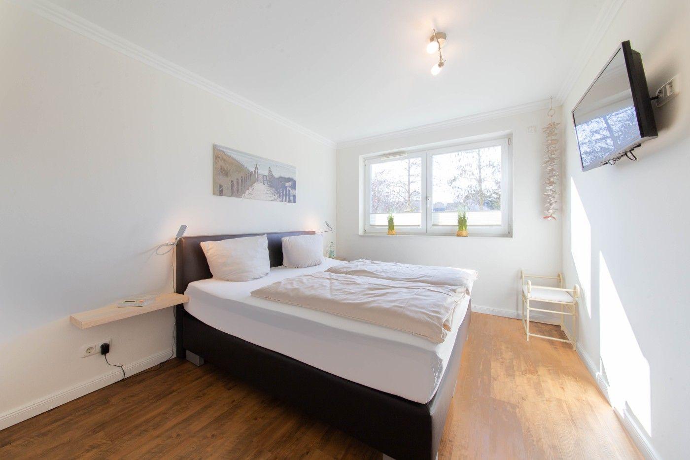 Schlafzimmer mit Doppelbett, Fenster, TV und Holzboden.
