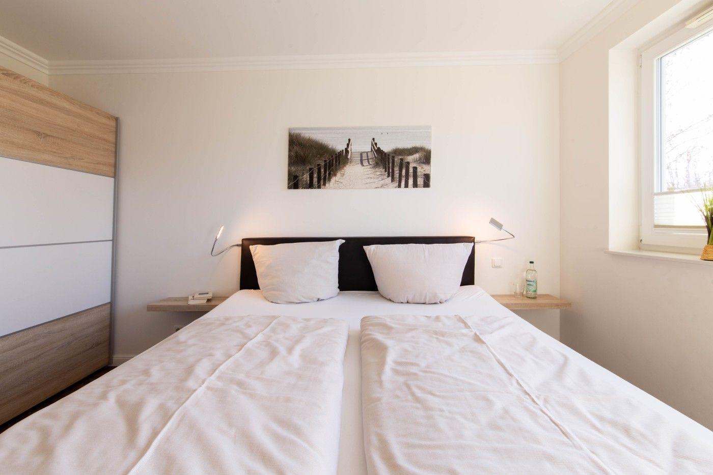 Schlafzimmer mit Doppelbett, Wandbild und Schrank. Fenster mit Pflanze.