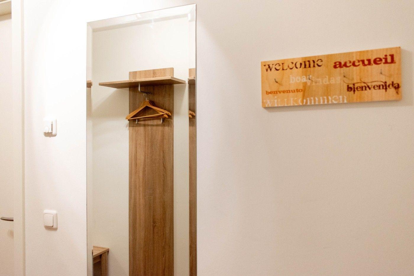 Hallenraum mit Kleiderständer und Willkommensschild in mehreren Sprachen an der Wand.