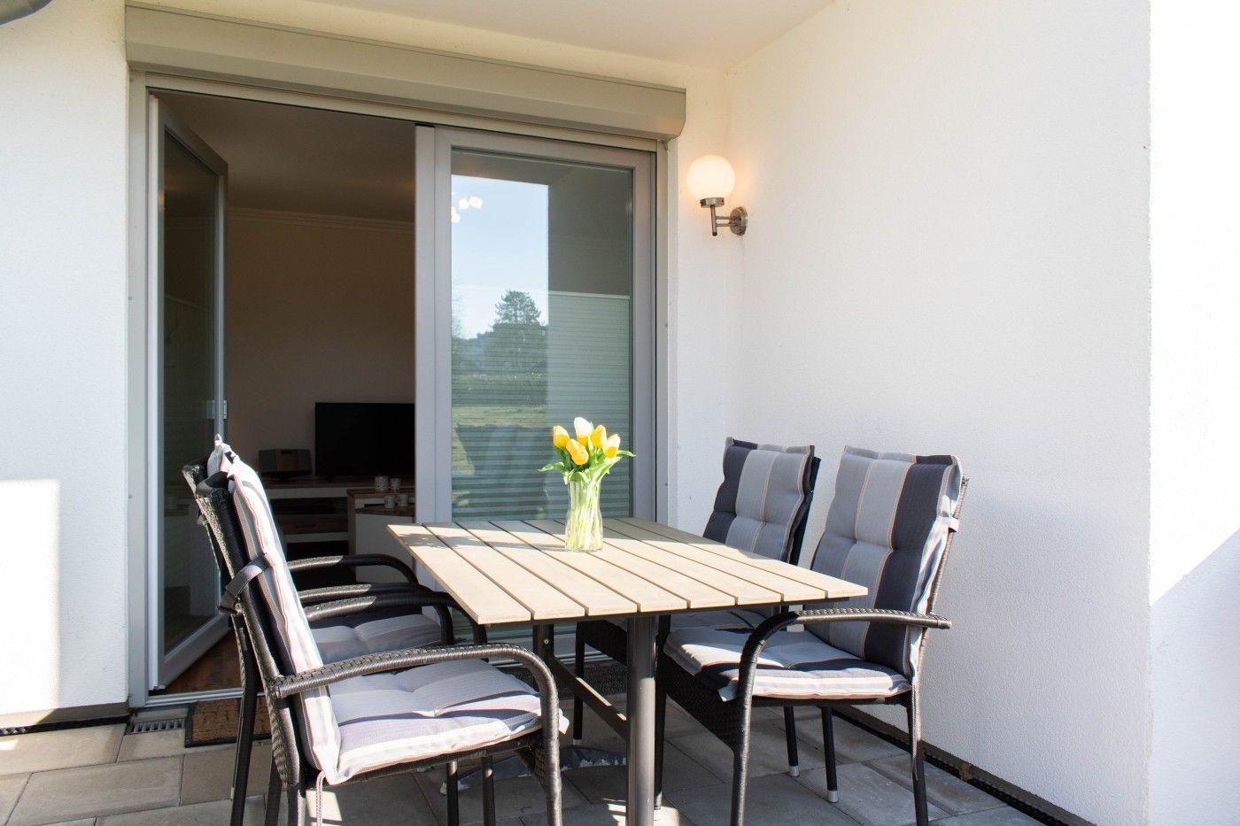 Terrasse mit Tisch und vier Stühlen, Blumen im Glas, Blick ins Haus.