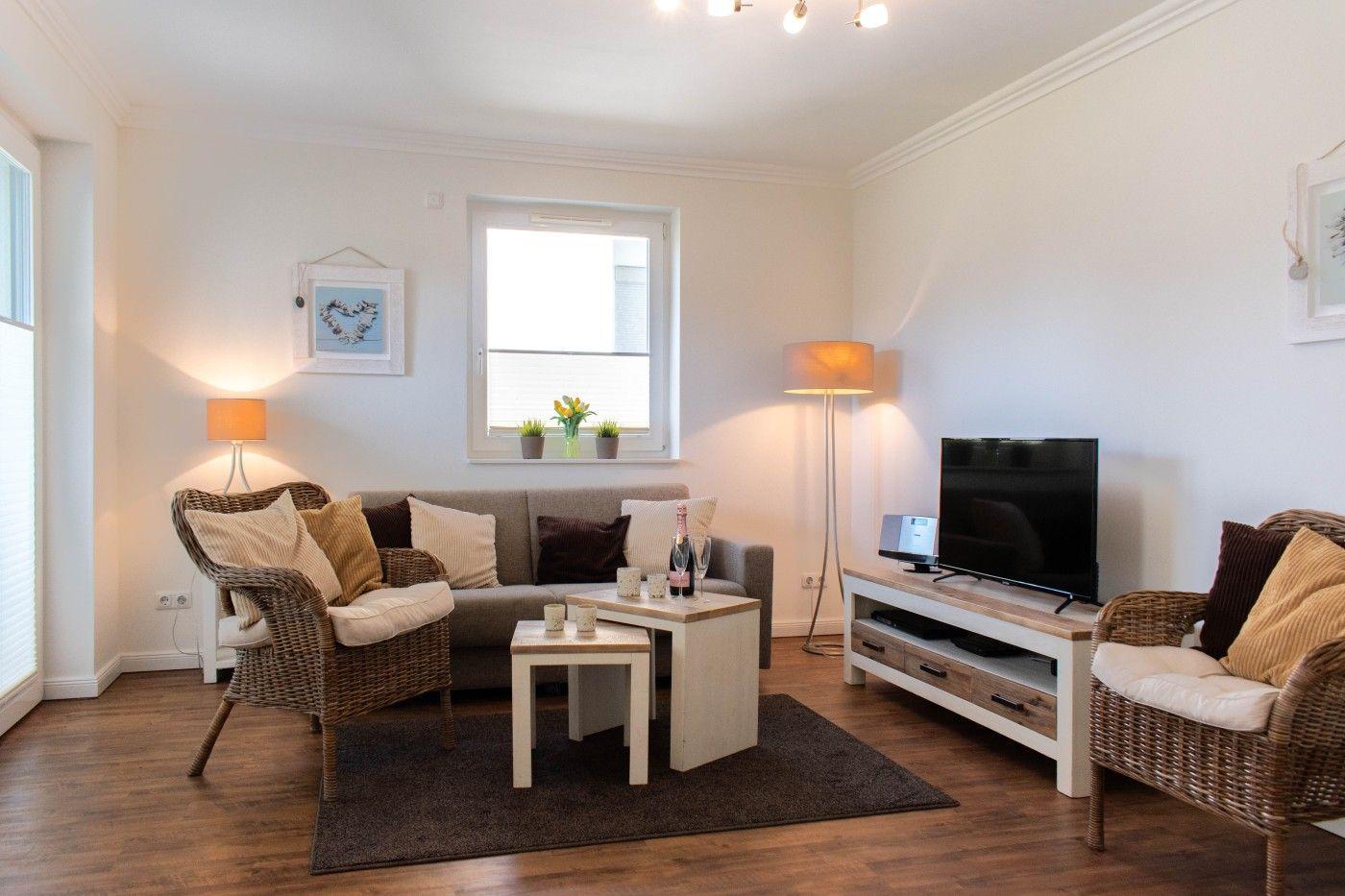 Wohnzimmer mit Sofa, zwei Sessel, TV und Tisch. Fenster und Lampen sorgen für Licht.