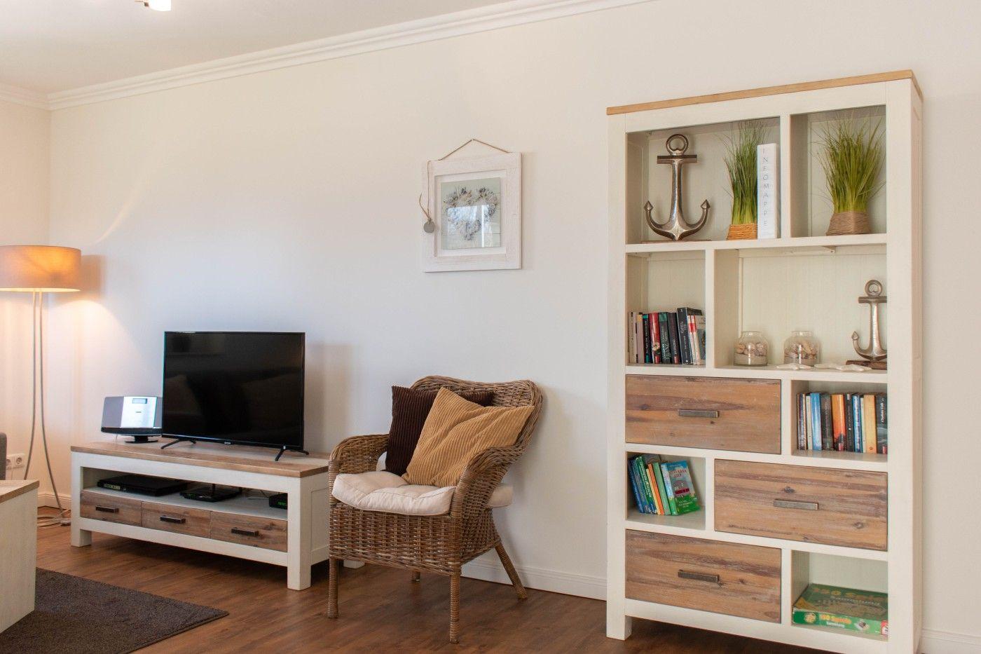 Wohnzimmer mit Fernseher, Wickerstuhl und Bücherregal mit Schiffsmotiven.