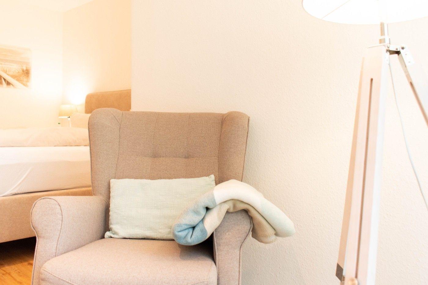 Ein Sessel mit Kissen und Decke neben einem Bett.