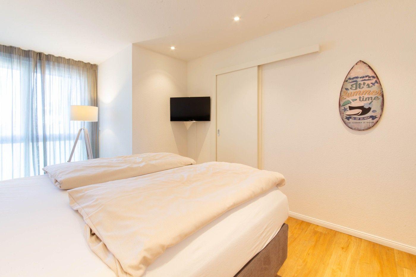 Schlafzimmer mit Bett, TV und Schiebetüren. Wanddekoration und Holzboden.