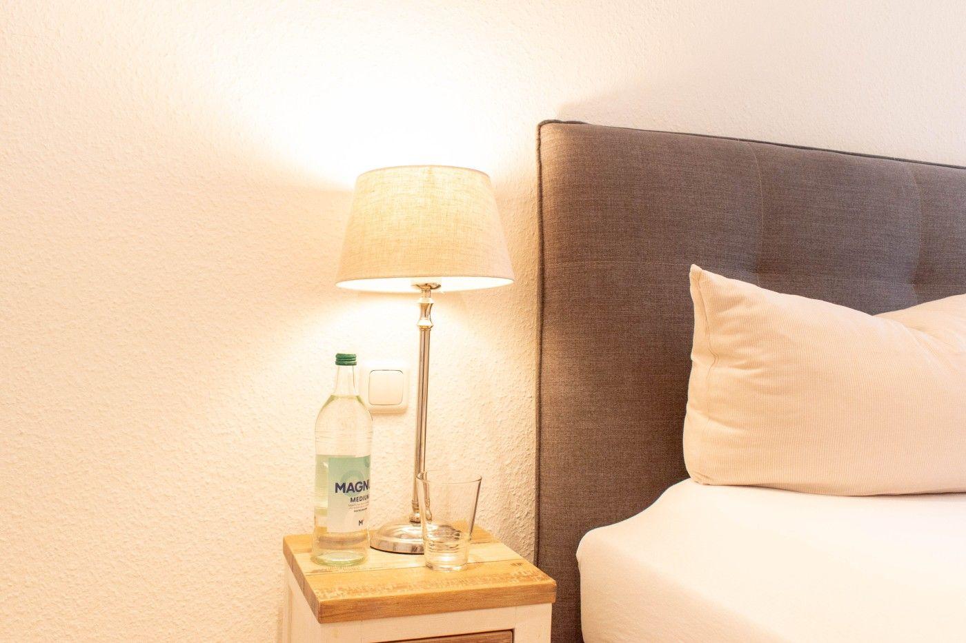 Bettkopfteil, Nachttisch mit Lampe, Glas und Flasche.