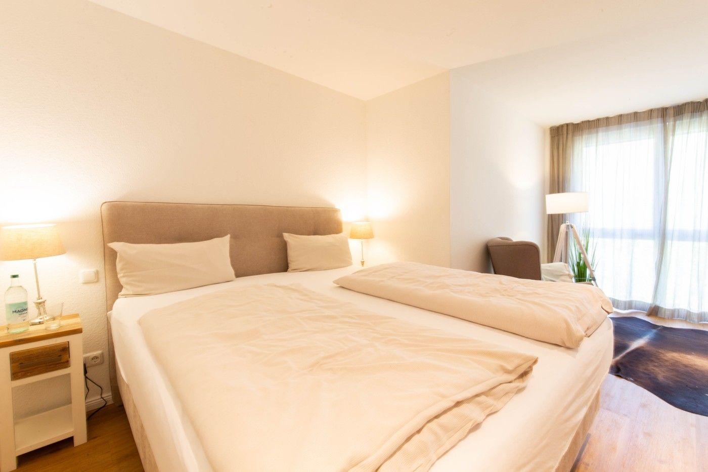 Ein Schlafzimmer mit Doppelbett, Nachttisch und Fenster mit Vorhängen.