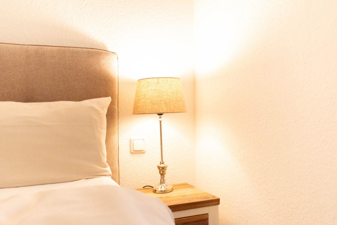 Bettkopfteil mit Kissen, Nachttisch und Stehlampe an der Wand.