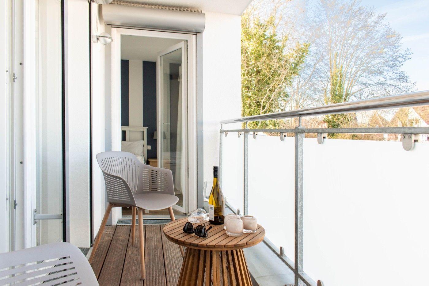 Terrasse mit Tisch, Stuhl und Weinflasche. Blick in das Schlafzimmer.
