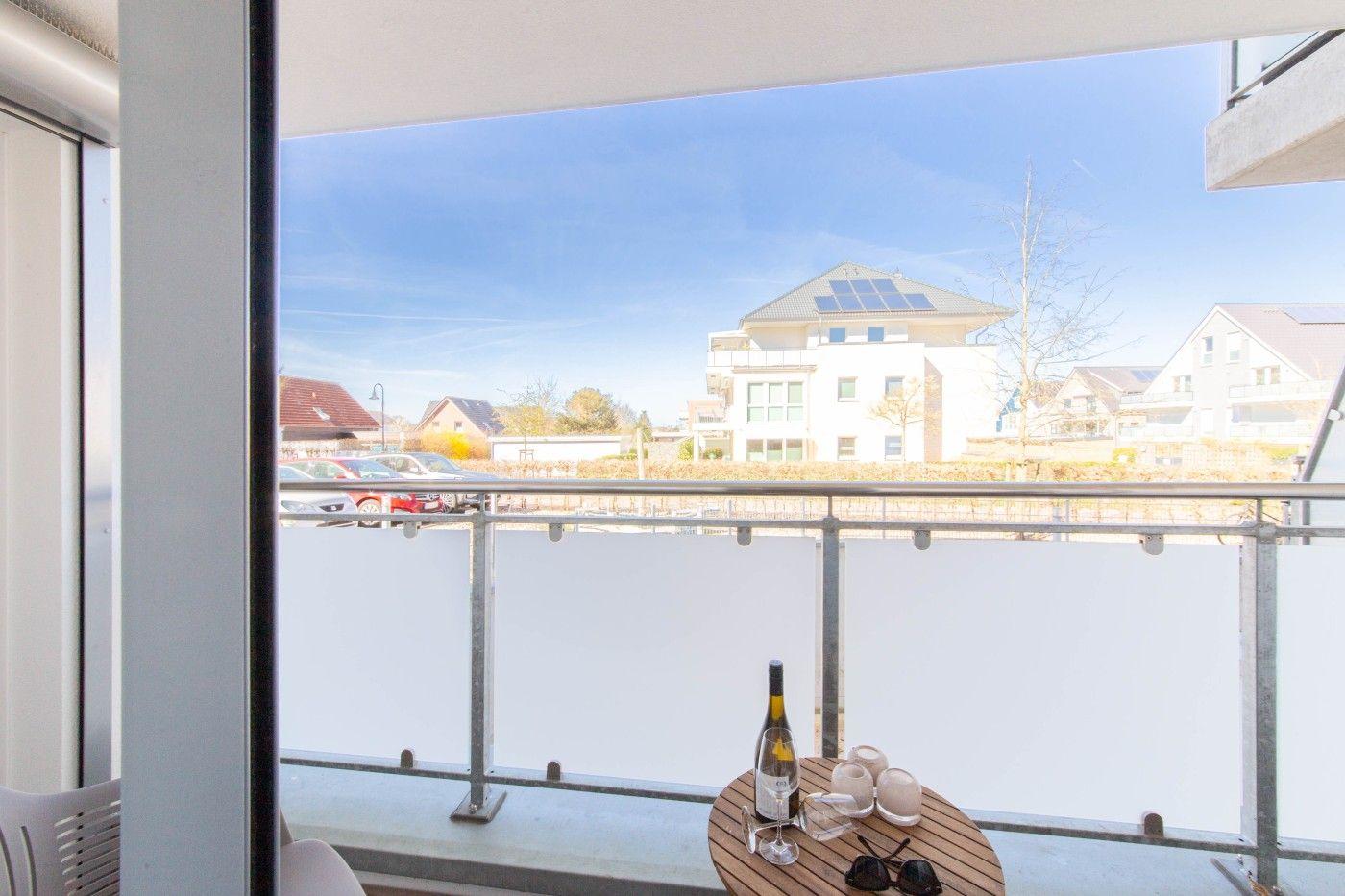 Terrasse mit Tisch, Wein und Sonnenschutz, Blick auf Wohnhäuser und Parkplatz.