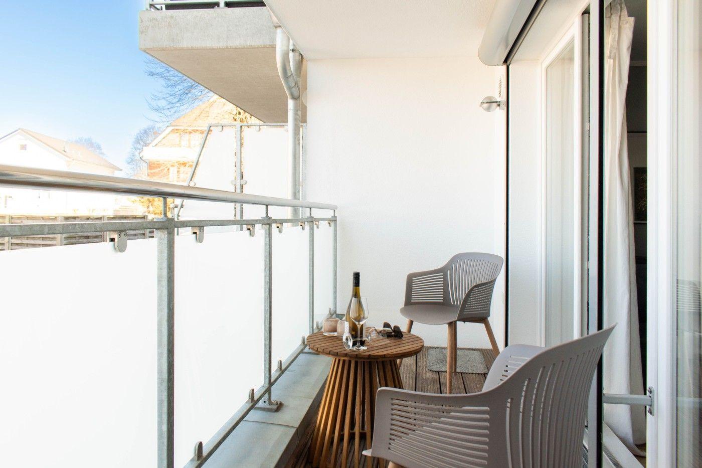 Terrasse mit Tisch, zwei Stühlen und Weinflasche. Blick auf angrenzende Gebäude.