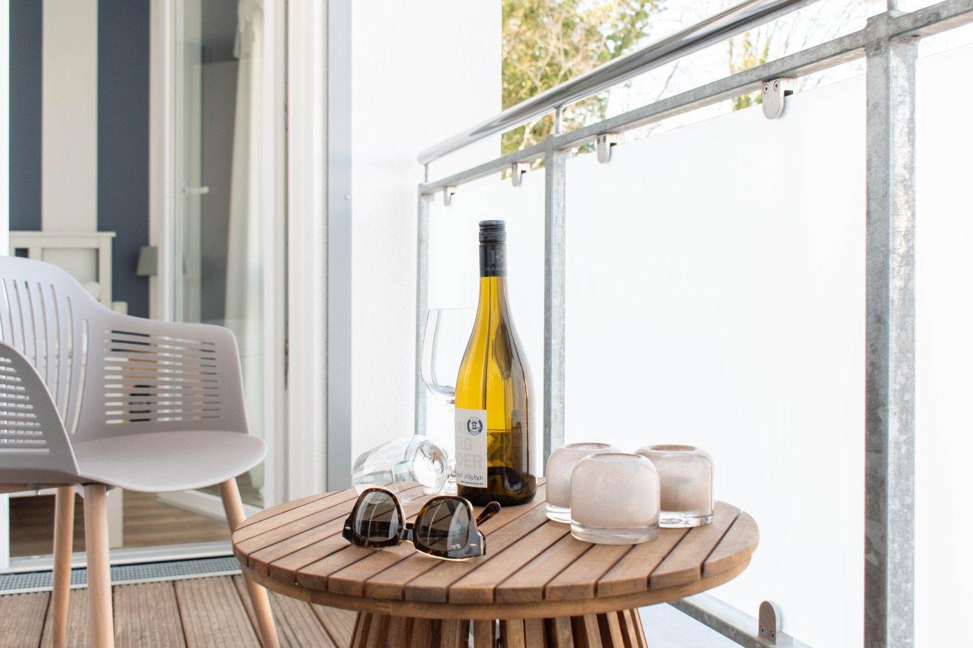 Auf der Terrasse steht ein runder Holztisch mit einer Weinflasche, Gläsern und Sonnenbrille.