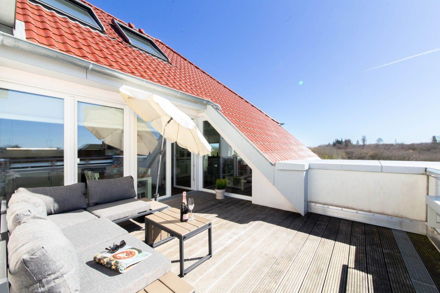 Terrasse mit Sofa, Tisch und Sonnenschirm unter rotem Dach.
