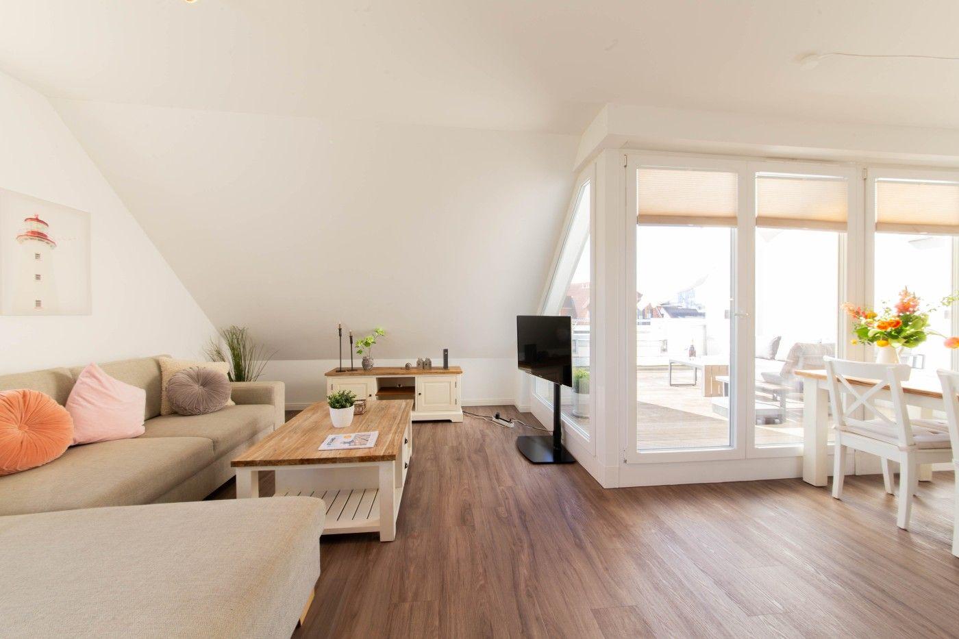 Wohn- und Essbereich mit Holzboden, Sofa, Fernseher und Blick auf Terrasse.