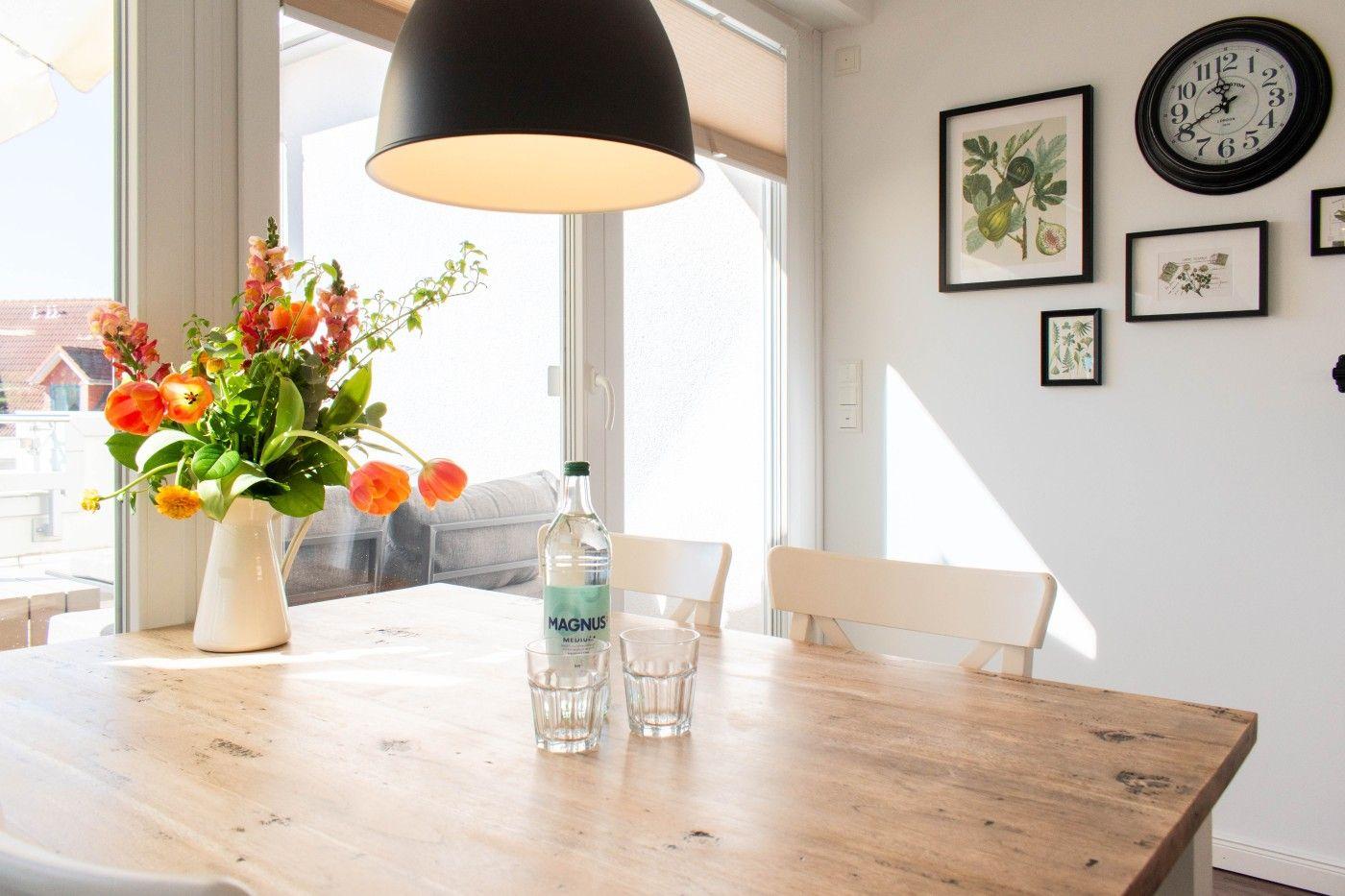 Esstisch mit Blumen und Flasche vor Fenster mit Blick auf Balkon.