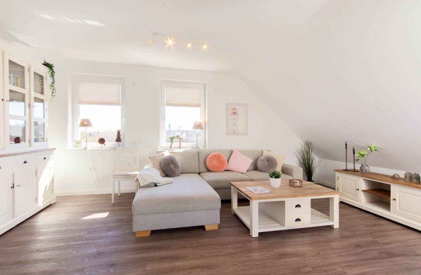Wohnzimmer mit Sofa, Couchtisch und Fenstern. Holzboden und weiße Möbel.