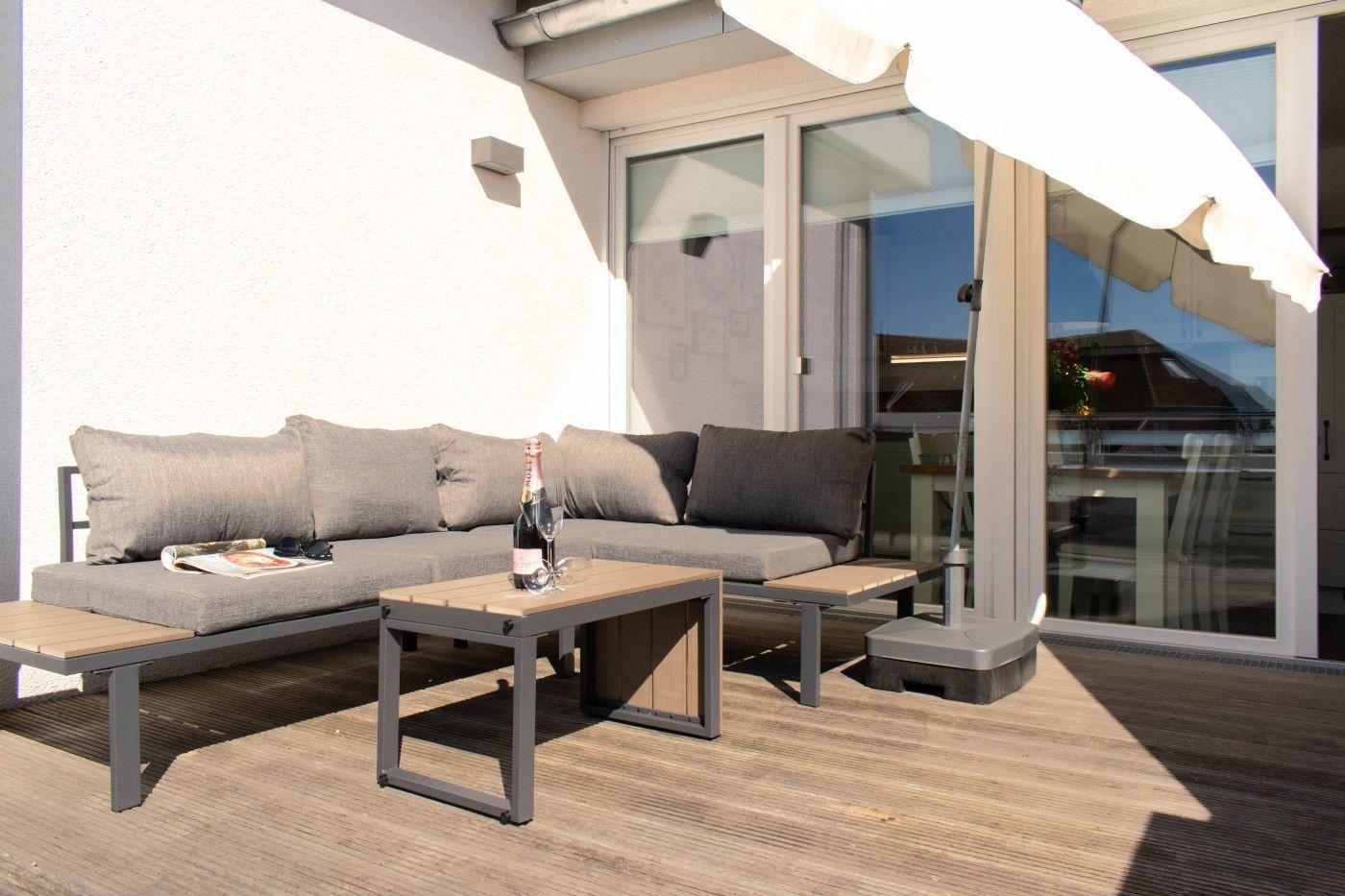 Terrasse mit Sitzbank, Tisch und Sonnenschirm. Durchgangstür führt ins Haus.