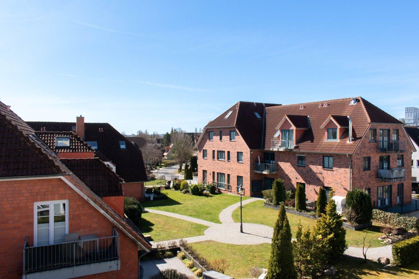 Rote Backsteinhäuser mit Dächern und Balkonen in grüner Umgebung.