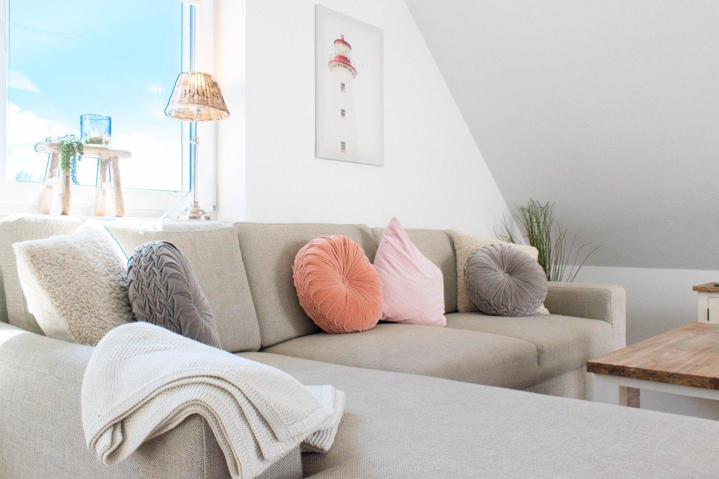 Ein Sofa mit Kissen und einer Decke vor einem Fenster mit Blick aufs Meer.
