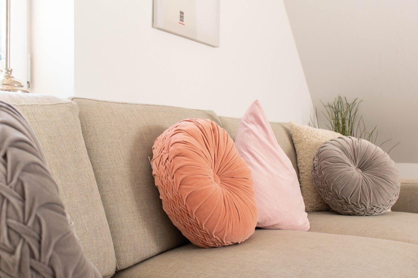 Ein Sofa mit runden Kissen in verschiedenen Farben und Texturen. Hintergrund: weiße Wand und Pflanze.