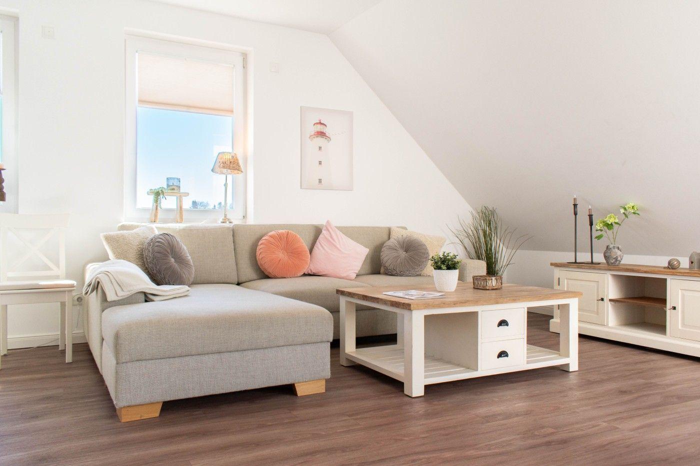 Wohnzimmer mit Sofa, Couchtisch und Fenster. Wandbild zeigt Leuchtturm.