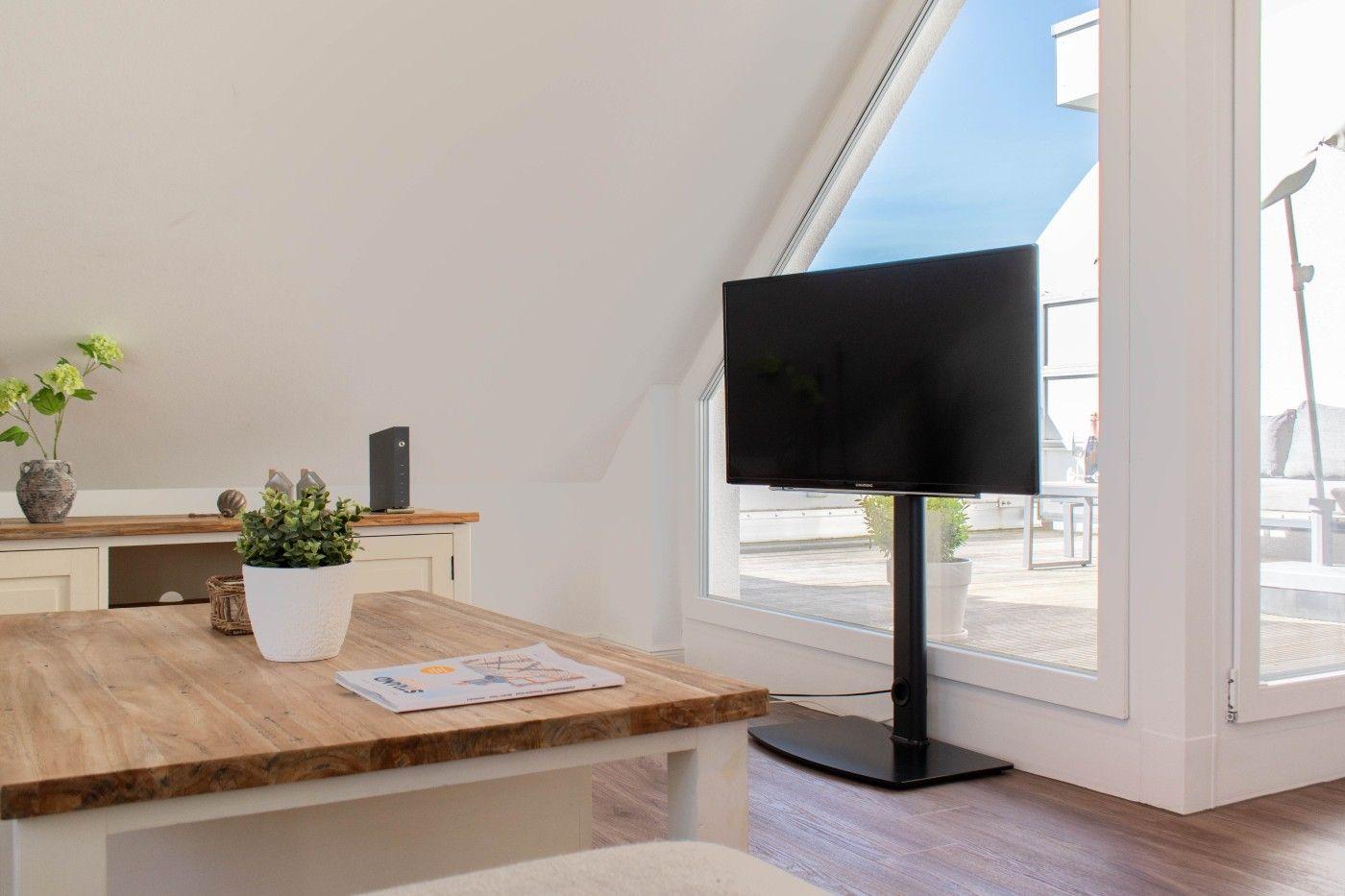 Ein Wohnraum mit TV-Ständer, Holztisch und großem Fenster zur Terrasse.