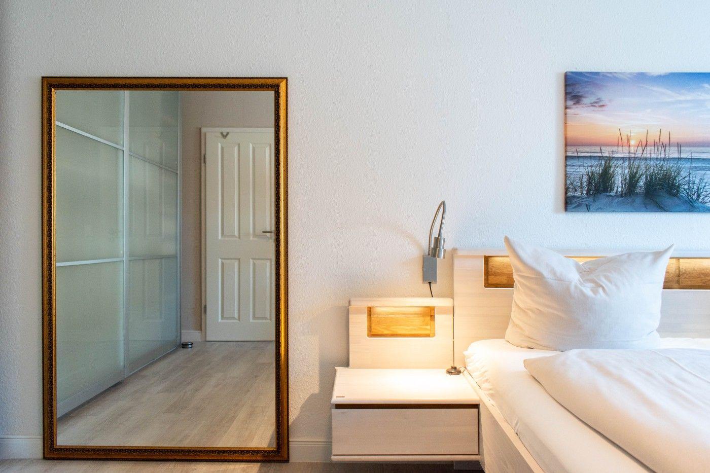 Schlafzimmer mit Bett, Nachttisch und Wandbild. Spiegel zeigt Schlafzimmer und Tür.