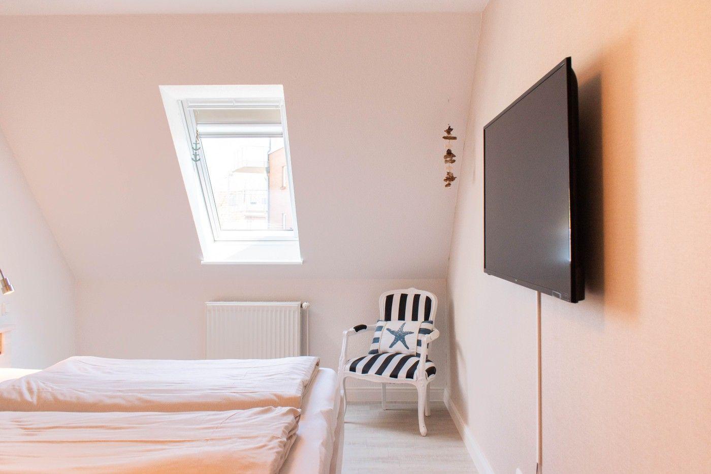 Schlafzimmer mit Dachschrägen, Dachfenster, Bett, Sessel und Wandfernseher.