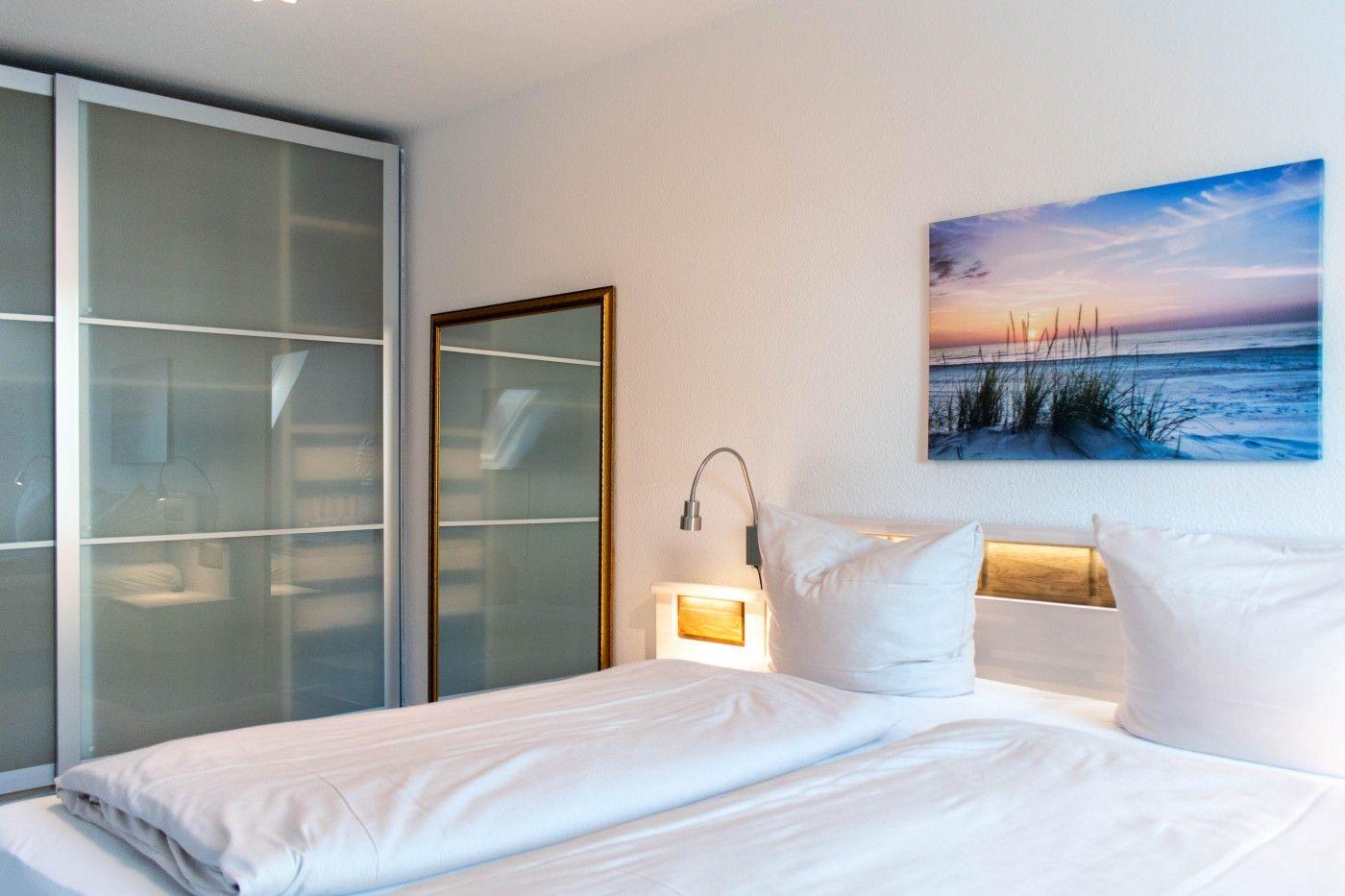 Schlafzimmer mit Doppelbett, Wandbild und Schwebetüren.