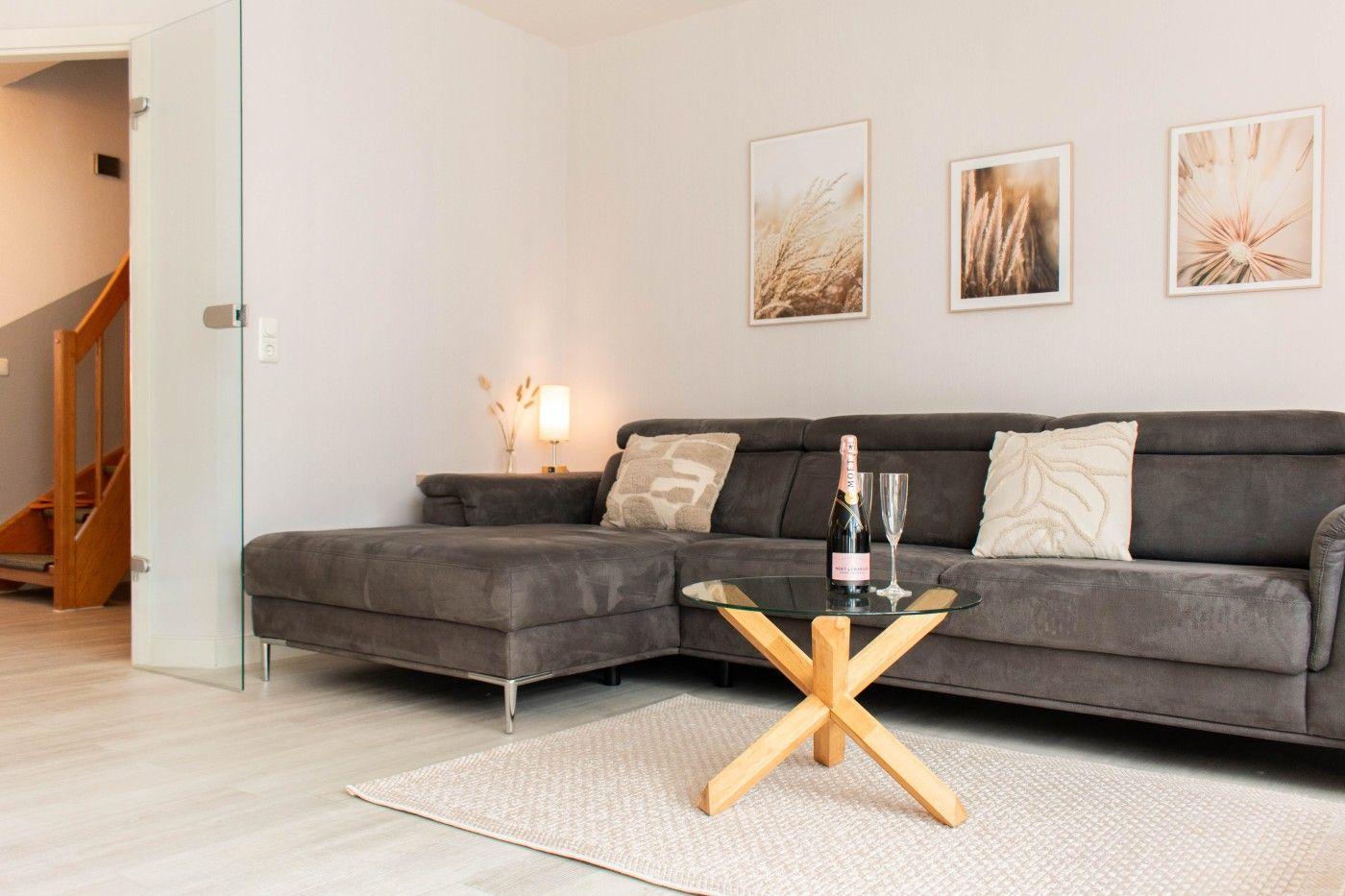 Wohnzimmer mit grauem Sofa, Glas-Tisch und drei Wandbildern.