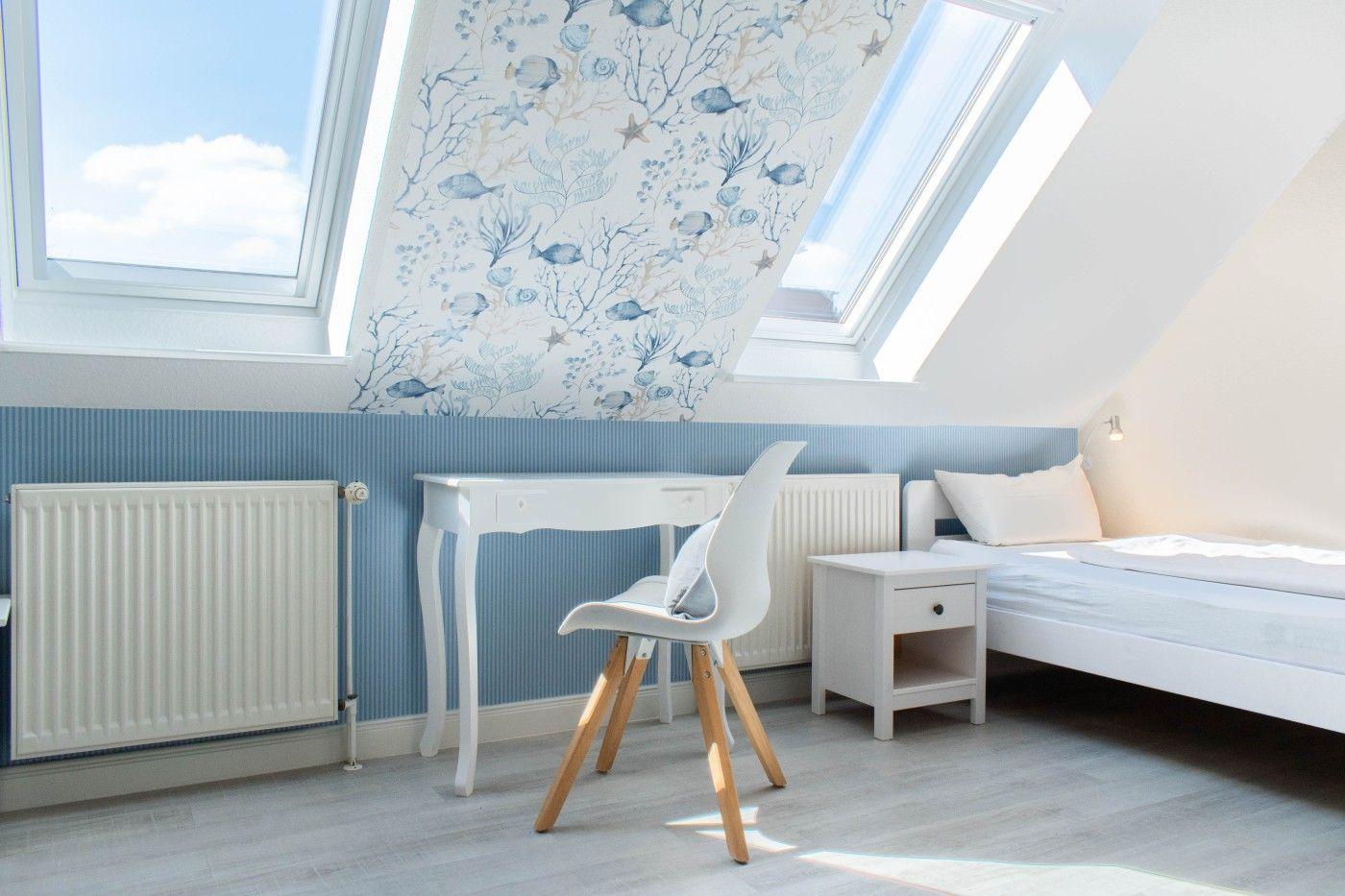 Schlafzimmer mit Dachfenstern, Bett, Schreibtisch und Stuhl.
