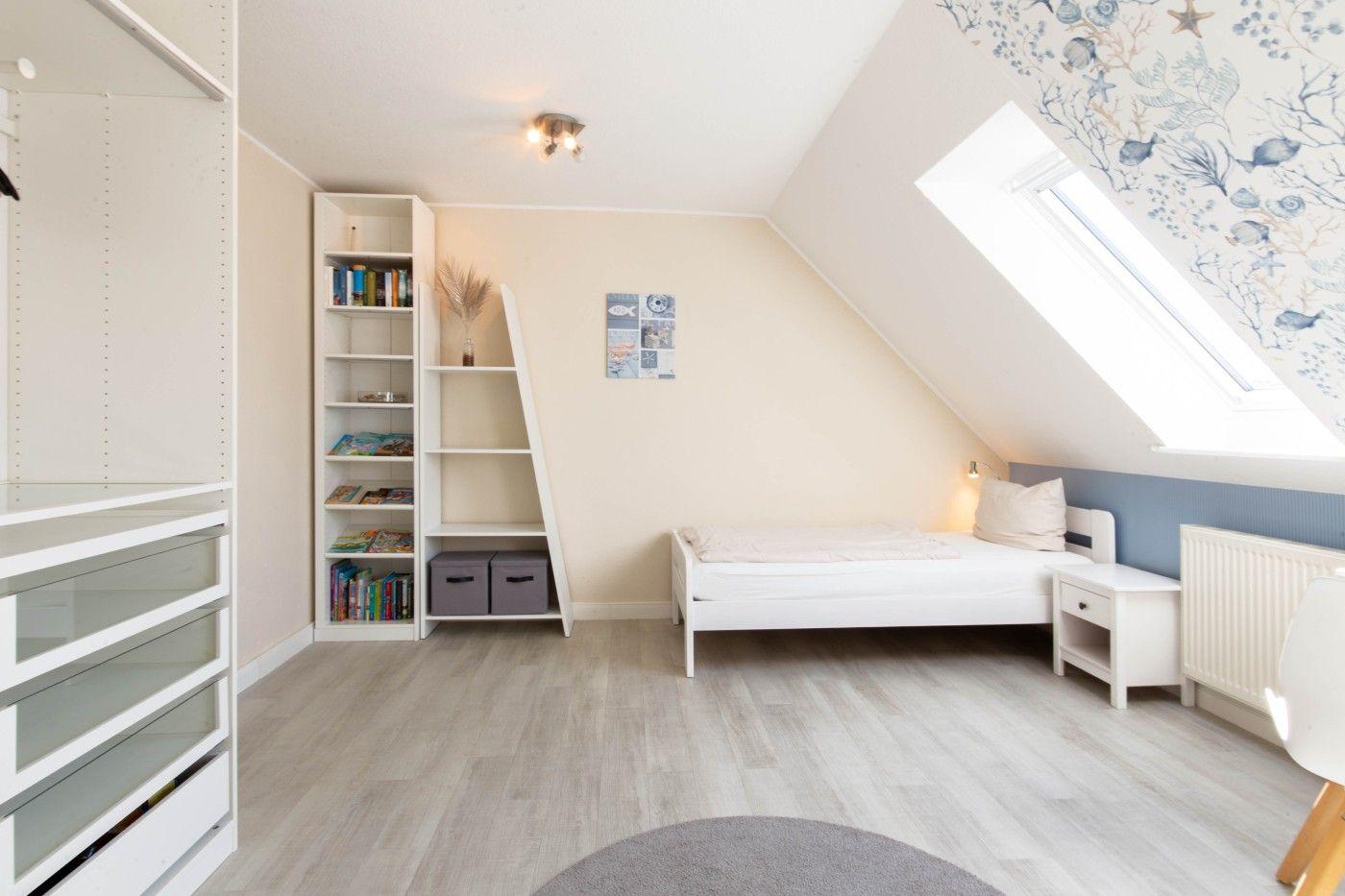 Dachgeschosszimmer mit Dachschrägen, Bett, Kleiderschrank und Bücherregal.
