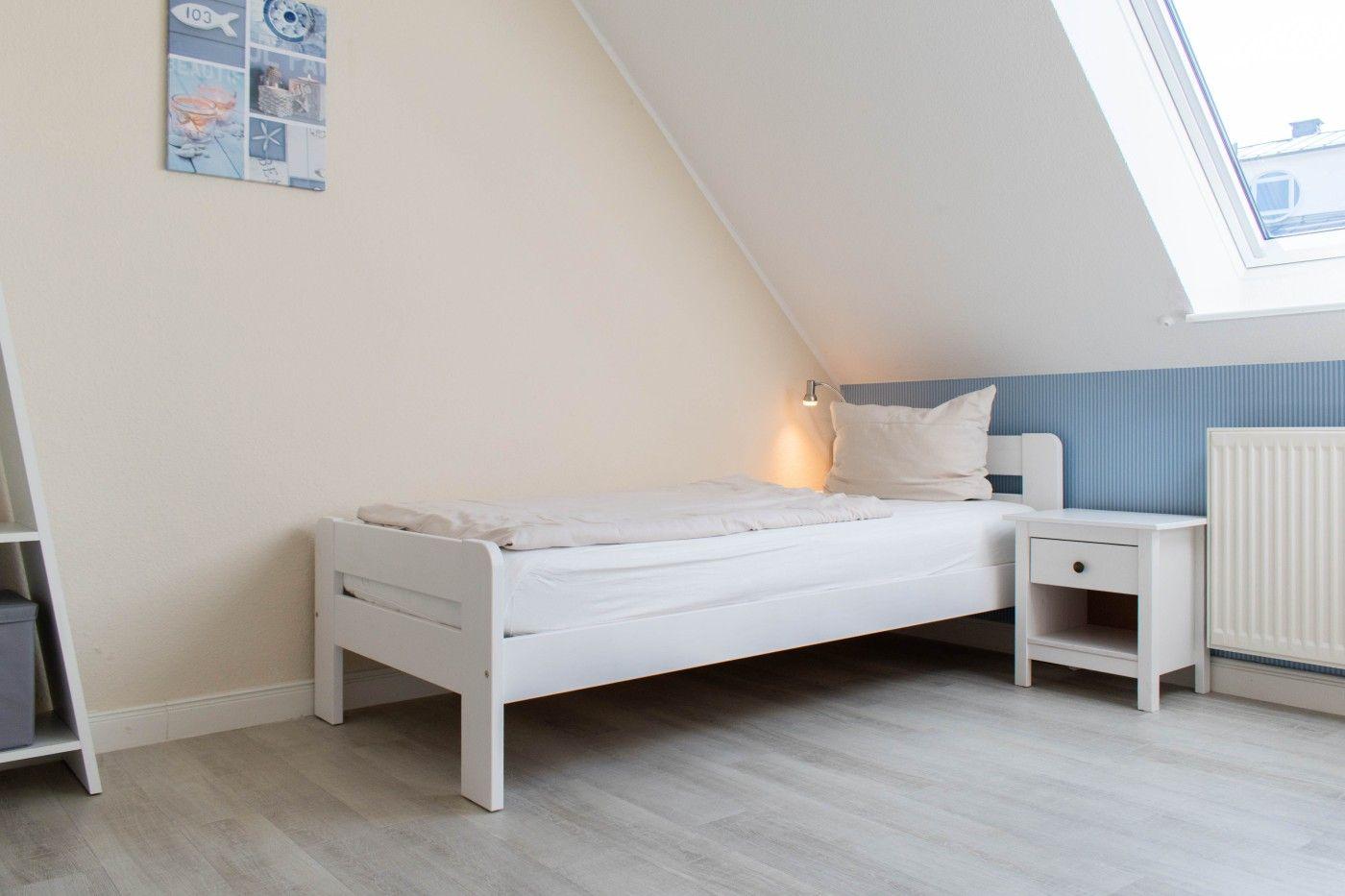 Ein Schlafzimmer mit weißem Bett, Nachttisch und Dachfenster.
