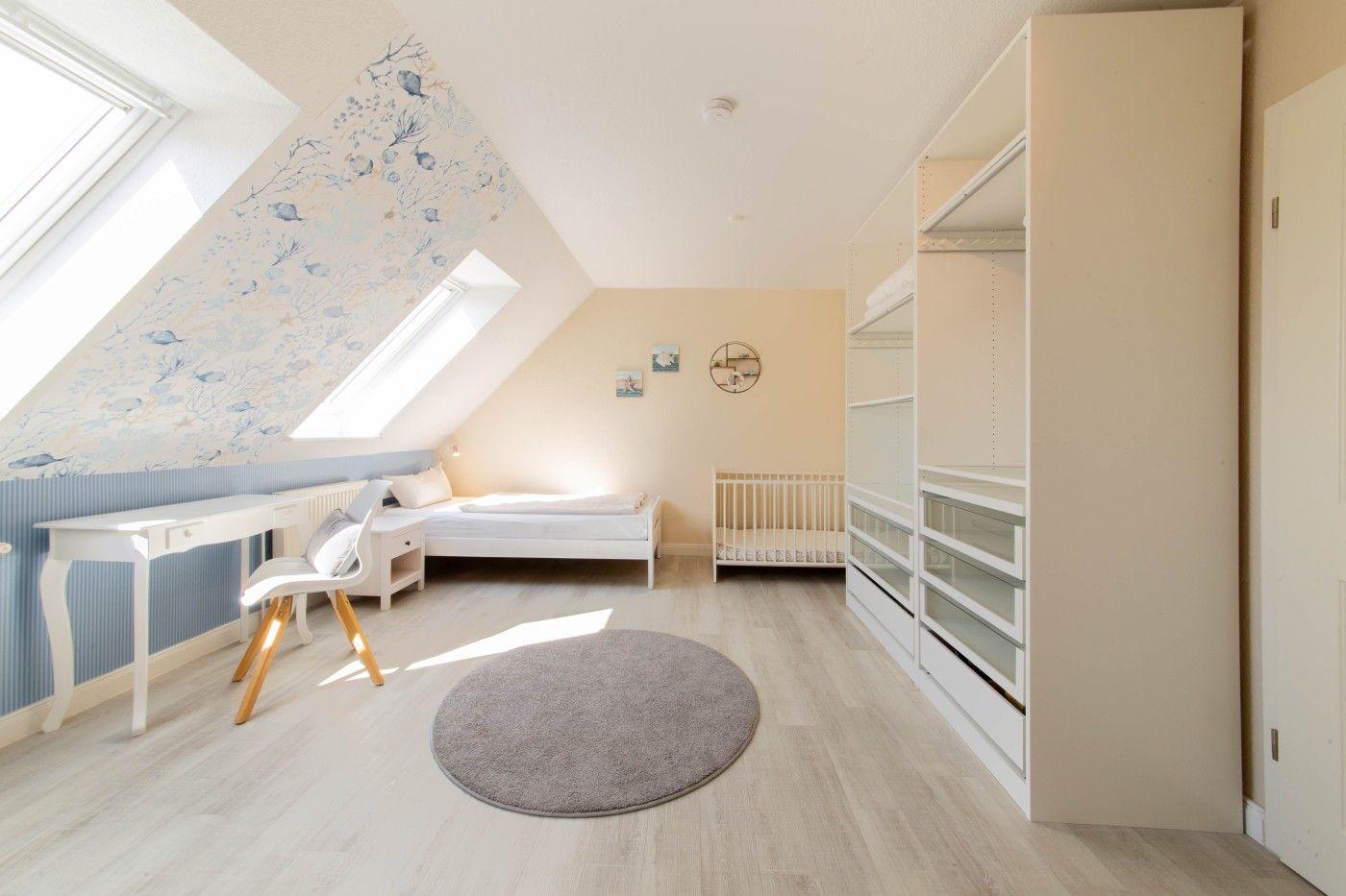 Dachgeschosszimmer mit Babybett, Schreibtisch und Kleiderschrank.